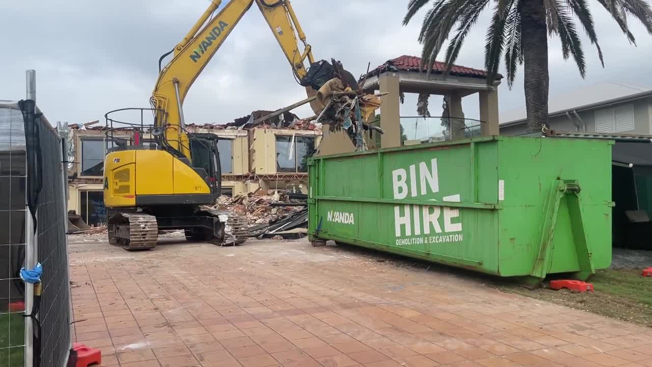 Excavator carefully picks and places demo waste into piles and into the skip for removal from site.